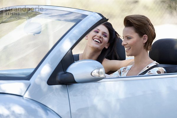 Zwei Frauen  die in einem Cabriolet lachen.