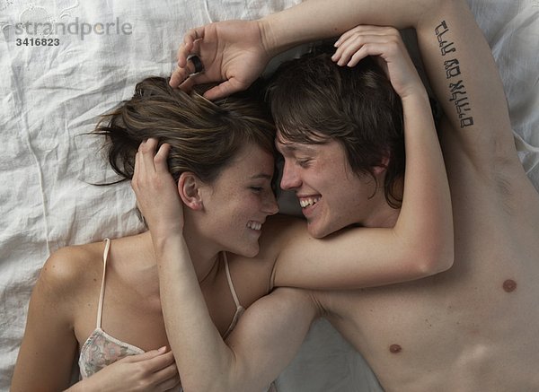 Glückliches junges Paar auf dem Bett liegend