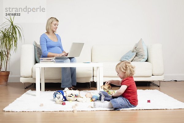 Frau auf einem Laptop zu Hause mit Kleinkind