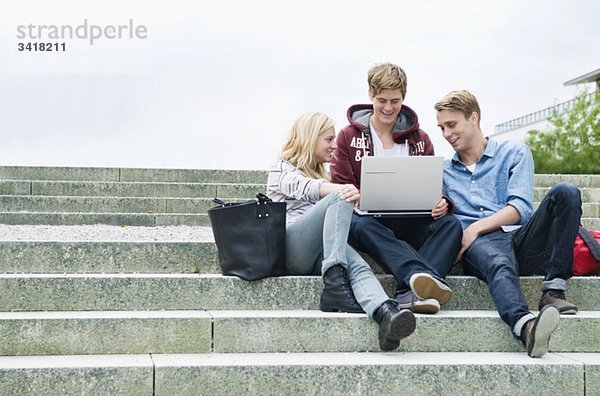 Drei Studenten sitzen in einer Steintreppe mit Laptop