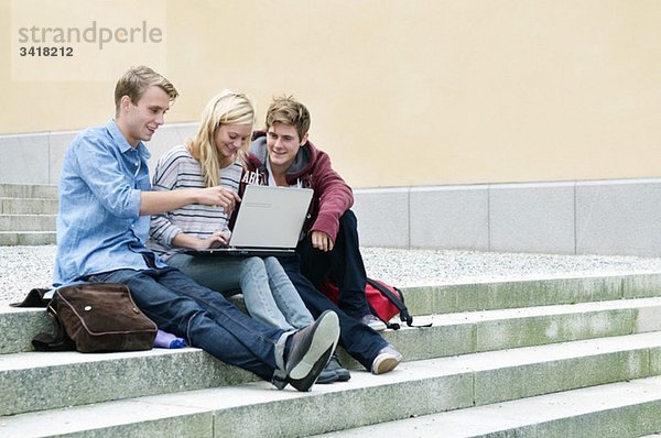 Drei Studenten sitzen auf einer Steintreppe mit Laptop