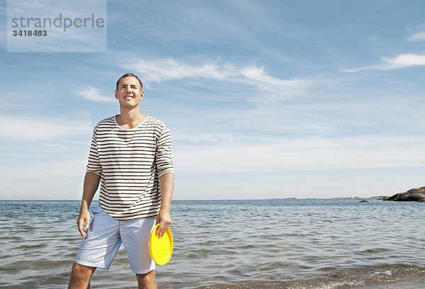 Mann steht am Strand und hält ein Frisbee.