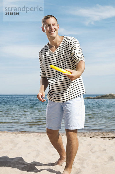 Ein Mann am Strand hält ein Frisbee.
