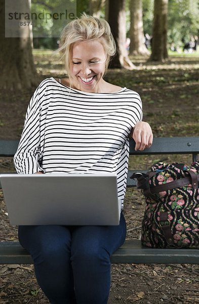 Glückliches Mädchen auf der Bank mit Computer