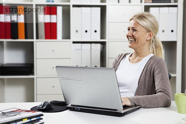 Glückliche Geschäftsfrau sitzend am Laptop