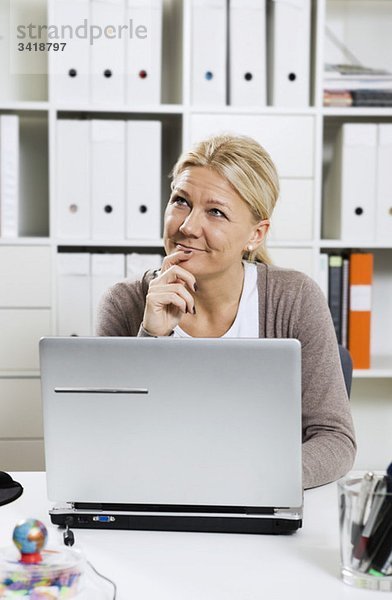 Frau sitzt am Schreibtisch mit Laptop