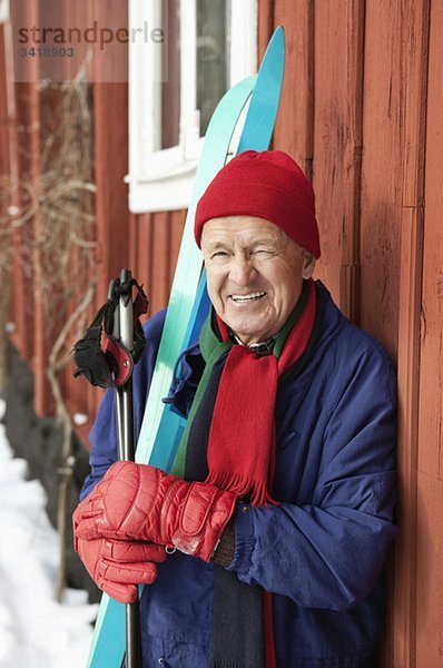 Nahaufnahme eines glücklichen Mannes  der draußen steht und Skier hält.