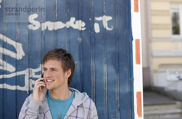 Junger Mann telefoniert vor einem Container stehend