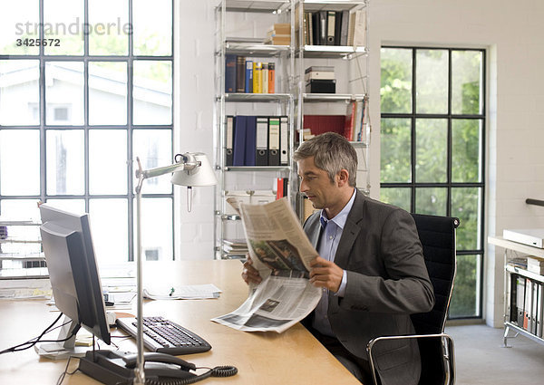 Geschäftsmann liest eine Zeitung am Schreibtisch