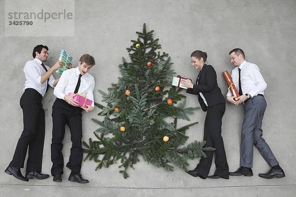 Vier Geschäftsleute mit Weihnachtsgeschenken rund um den Weihnachtsbaum  erhöhte Ansicht