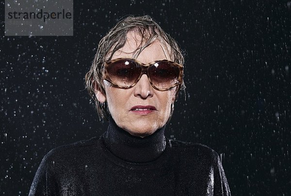 Frau steht im Regen und trägt eine Sonnenbrille.