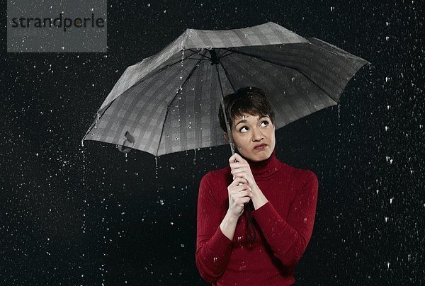 Frau steht im Regen  hält Regenschirm.