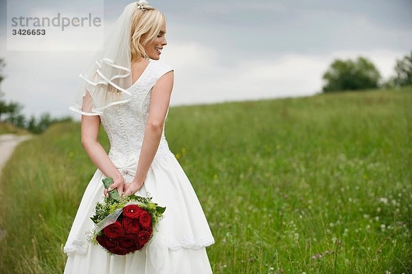Die Braut hält einen Blumenstrauß hinter ihrem Rücken und lächelt.