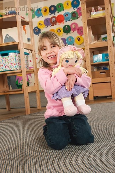 Deutschland  Mädchen (4-5) im Kinderzimmer mit Puppe  lachend  Portrait
