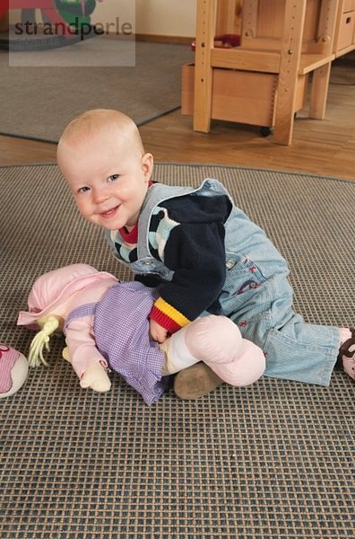 Deutschland  Baby Mädchen (12-17 Monate) im Kinderzimmer  mit Puppe spielen  lächeln  Portrait
