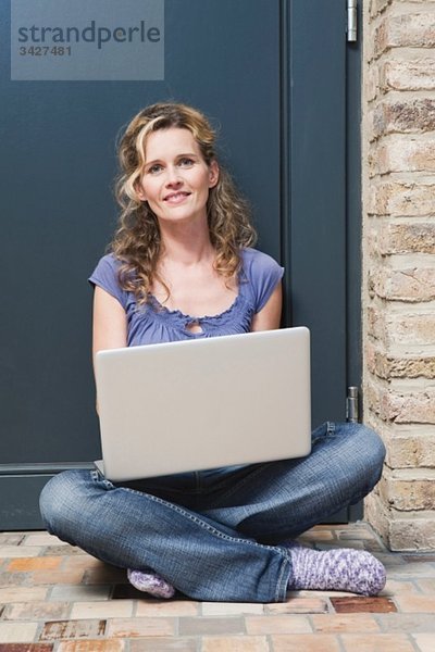 Frau vor der Tür sitzend mit Laptop  lächelnd  Porträt