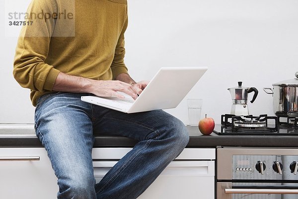 Mann auf Küchenarbeitsplatte sitzend  mit Laptop