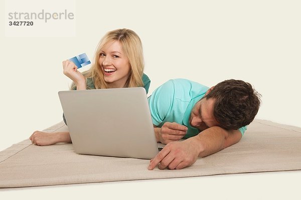 Paar liegend mit Laptop  Mann schlafend und Frau mit Kreditkarte