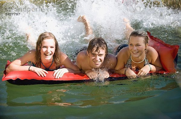 Österreich  Salzburger Land  Jugendliche (14-15) auf Luftmatratze Spritzwasser  Lachen  Portrait