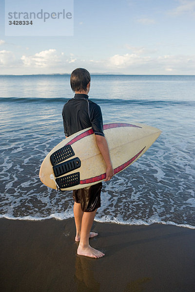 Auckland  junger Mann mit Surfbrett am Muriwai Beach