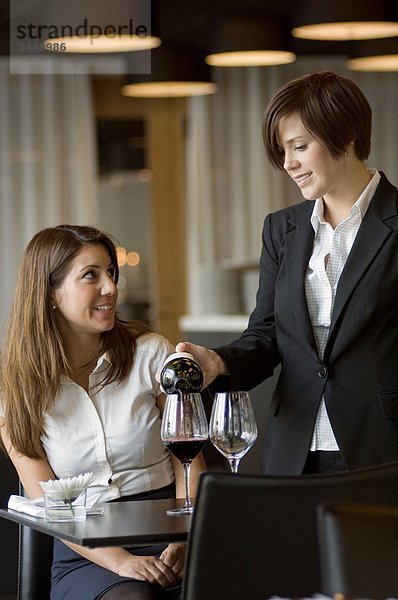 Waitress serving Wein für Frau am Tisch  lächelnd
