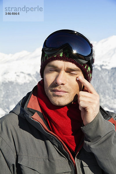 Junger Mann in Skikleidung mit Feuchtigkeitscreme im Gesicht