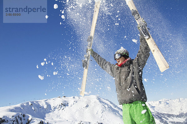 Junger Mann hält seine Skier über den Kopf.