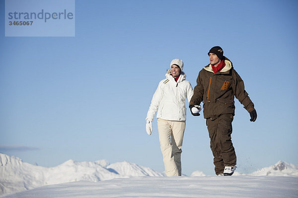 Junges Paar hält sich an den Händen  geht im Schnee spazieren