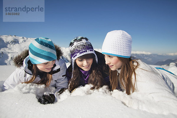 Drei Teenagermädchen in Skikleidung  im Schnee liegend