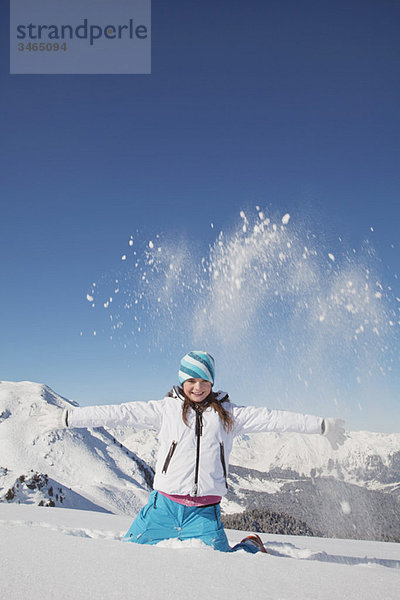 Mädchen in Skikleidung  Schnee in die Luft werfen