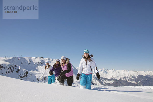 Vier Teenagermädchen in Skikleidung  die im Schnee spazieren gehen.