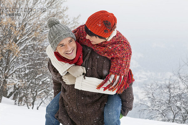 Junger Mann gibt seiner Freundin Huckepack im Schnee