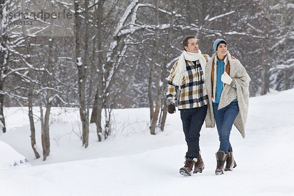 Junges Paar umarmend  im Schnee spazieren gehend