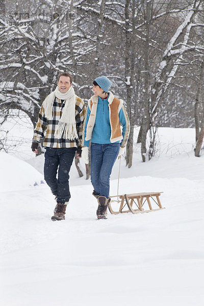 Junges Paar  das im Schnee läuft und einen Schlitten zieht.