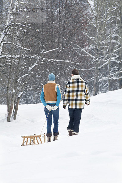 Junges Paar  das im Schnee läuft und einen Schlitten zieht  Rückansicht