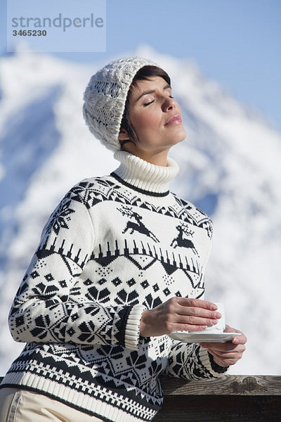 Junge Frau mit Kaffeetasse  Wintersonne genießen  Berge im Hintergrund