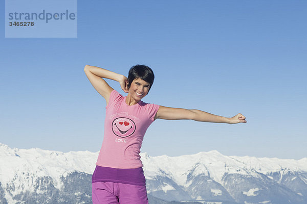Junge Frau mit erhobenen Armen  lächelnd vor der Kamera  Berge im Hintergrund
