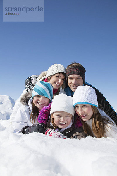 Glückliche Familie im Schnee liegend  lächelnd vor der Kamera