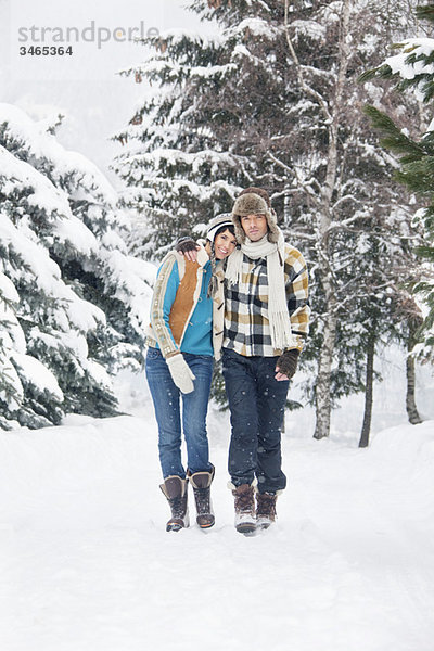 Junges Paar umarmend  im Schnee spazieren gehend