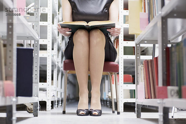 Eine Frau  die in einer Bibliothek mit einem Buch sitzt  konzentriert sich auf den Mittelteil und den unteren Teil.