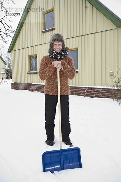 Ein Mann  der sich auf eine Schneeschaufel stützt  um Schnee zu schaufeln.