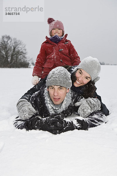 Eine dreiköpfige Familie  die im Schnee spielt.