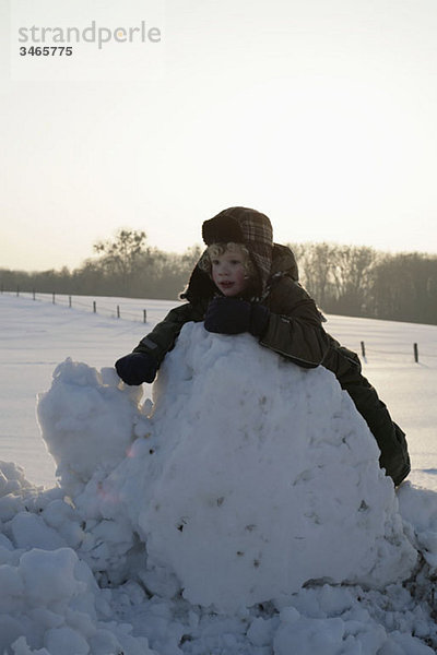 Ein Kind  das sich gegen einen Haufen Schnee lehnt.
