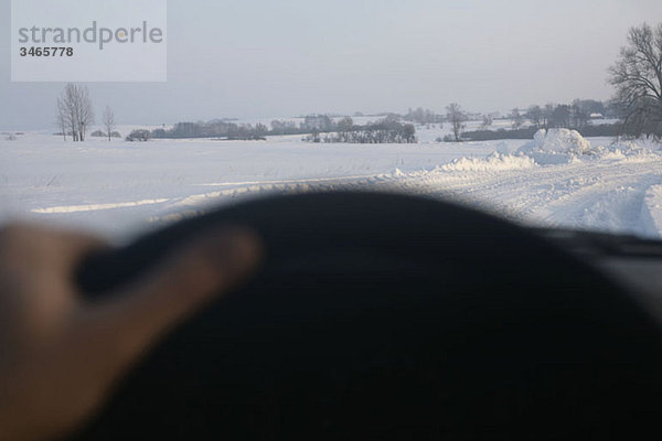 Blick auf die schneebedeckte Landstraße durch die Windschutzscheibe des Autos