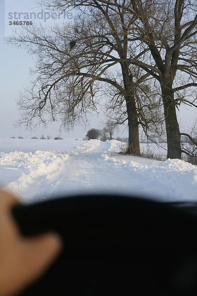 Blick auf die schneebedeckte Landstraße durch die Windschutzscheibe des Autos