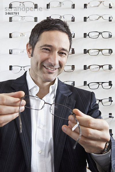Ein lächelnder Optiker hält eine Brille vor die Kamera in einem Brillengeschäft.
