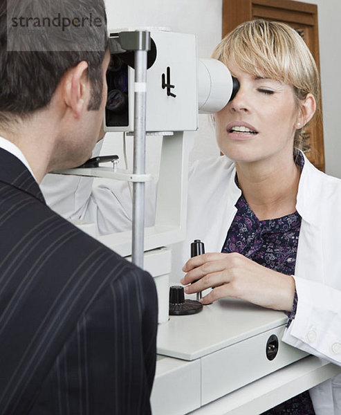 Ein Augenarzt untersucht einen Patienten mit einem Spaltlampen-Biomikroskop.