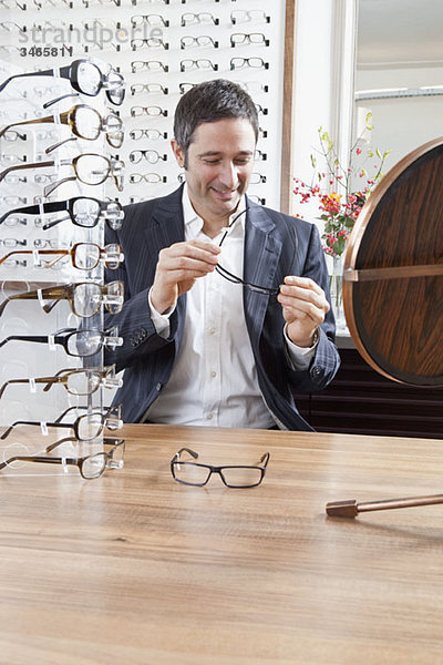 Ein reifer Mann  der eine Brille in einem Brillengeschäft auswählt.
