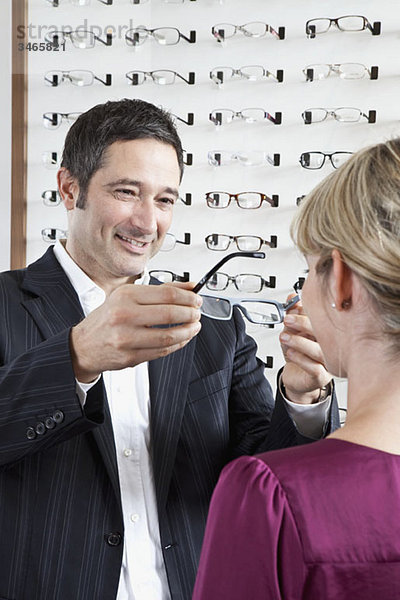 Ein Augenoptiker  der einem Kunden in einem Brillengeschäft eine Brille hält
