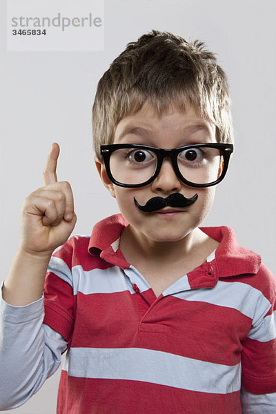 Ein junger verspielter Junge mit einer falschen Brille und einem falschen Schnurrbart.